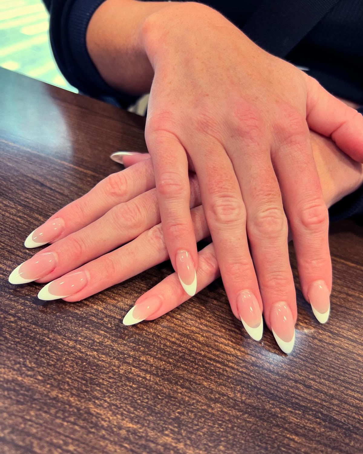 Soft French tips on medium almond nails, two hands resting on a table.